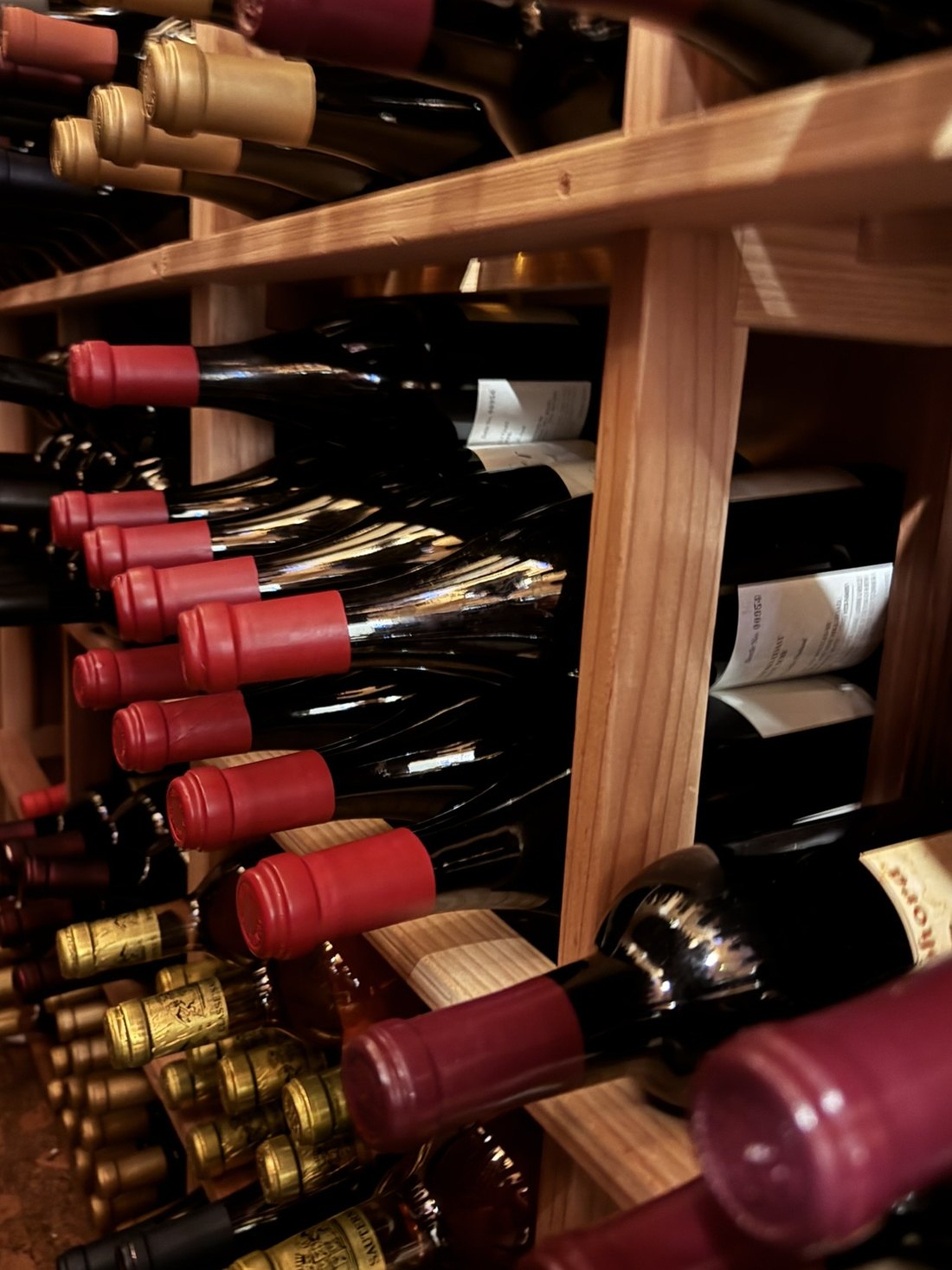 Rows of bottles resting on their sides in a wooden cellar rack, capsules facing out